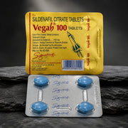 Vega 100 Sildenafil Citrate Tablets packaging shown with a yellow blister pack and a silver foil blister containing four blue tablets, set against a dark textured stone background.